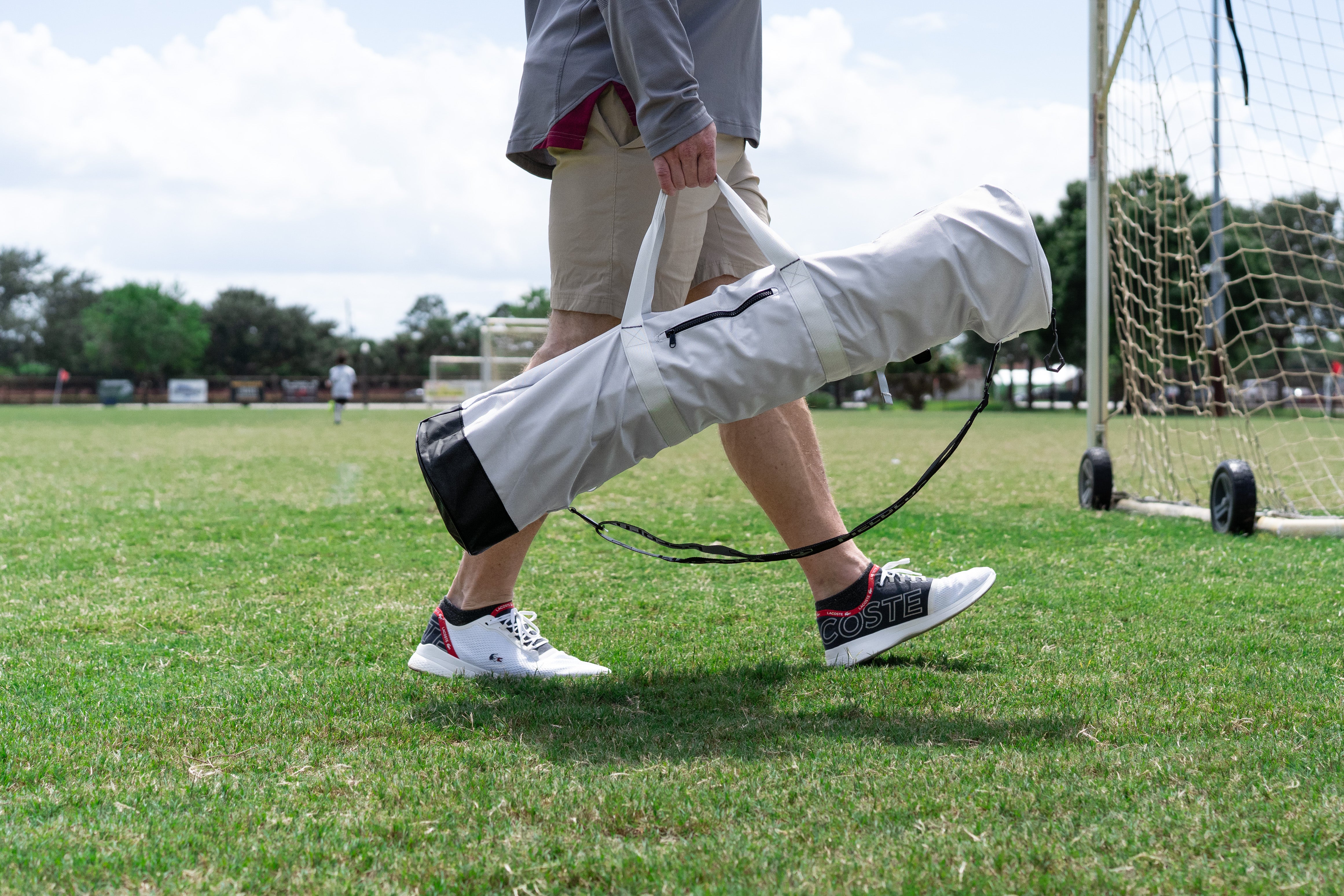 Person carrying a FieldLux bag by a soccer field with a soccer goal in the background